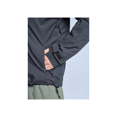 Close-up van zwarte jas met zijzak en trekkoord detail, gedragen met groene broek