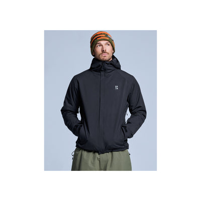 Man draagt zwarte softshell jas met capuchon en groene broek, winter outdoorkleding