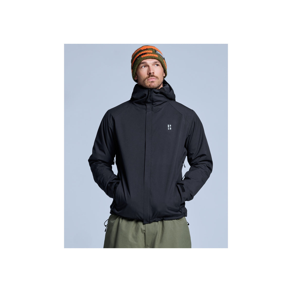 Man draagt zwarte softshell jas met capuchon en groene broek, winter outdoorkleding