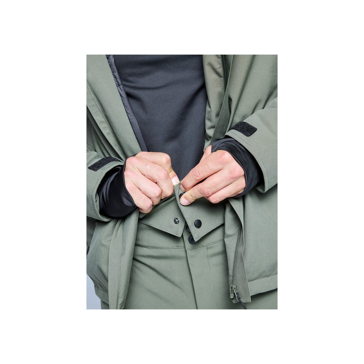 Close-up van handen die een groene jas dichtmaken met knopen, winterjas detail
