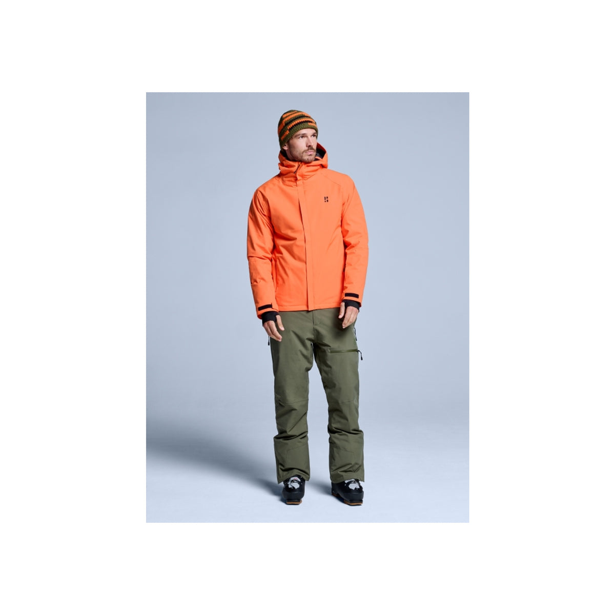 Man draagt oranje ski-jas en groene skibroek met bruine muts - winter sportkleding set