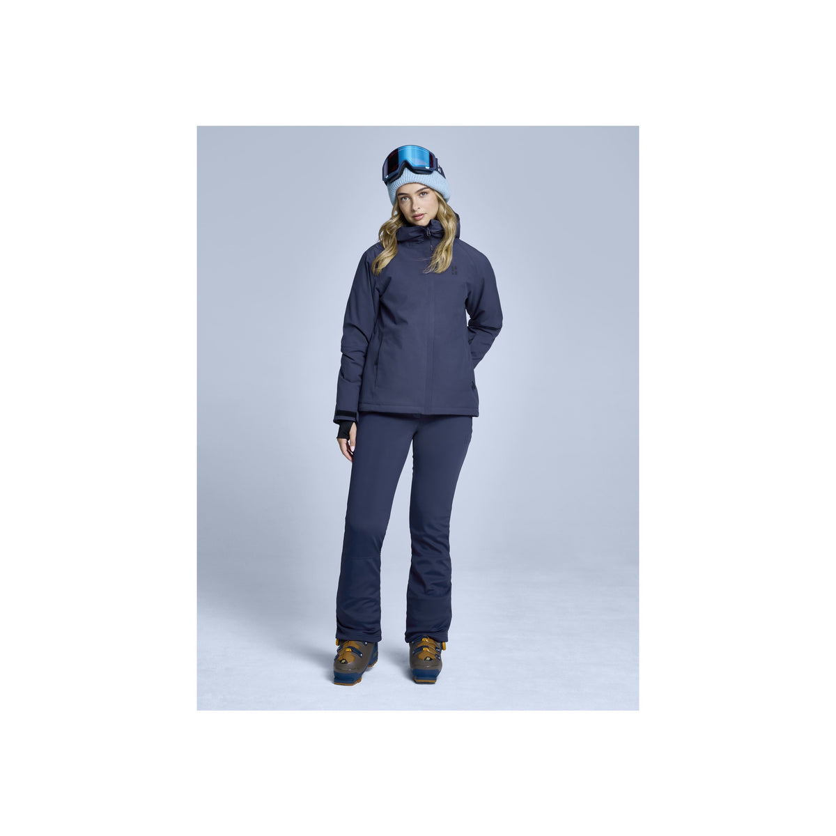 Vrouw in blauwe ski-jas en broek met muts en handschoenen, complete wintersport outfit