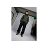 Model draagt groene hoodie en zwarte joggingbroek met sportschoenen in urban setting