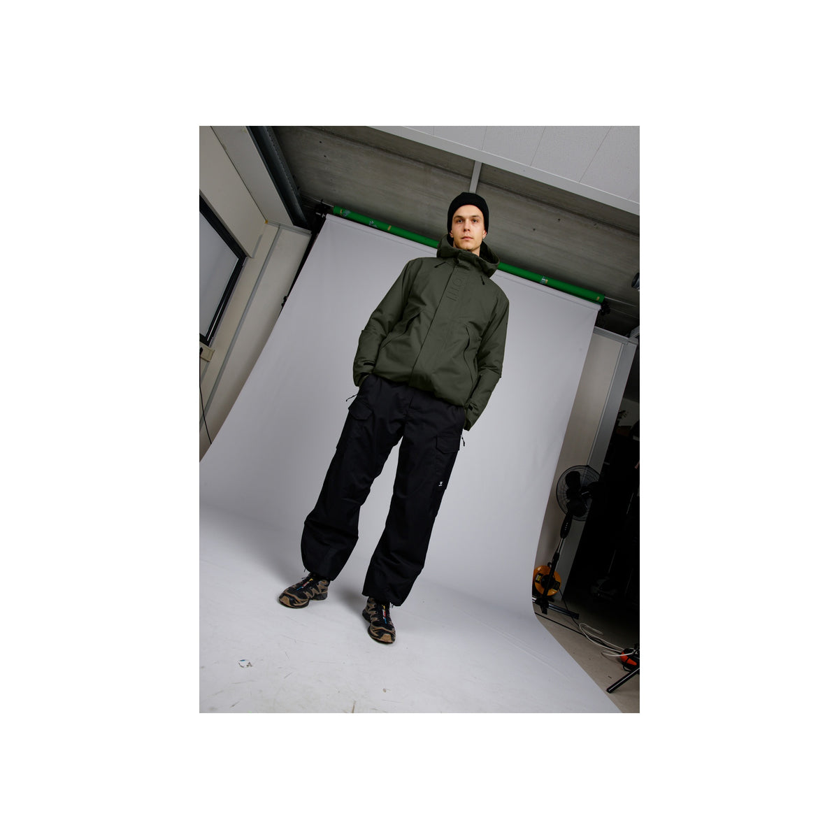 Model draagt groene hoodie en zwarte joggingbroek met sportschoenen in urban setting