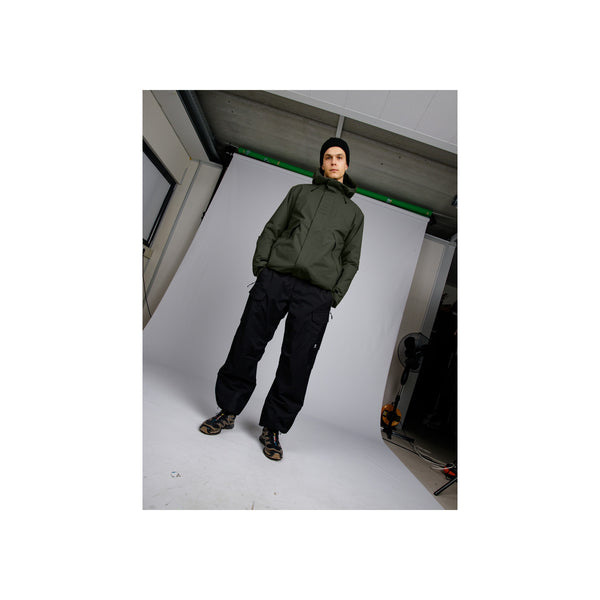 Model draagt groene hoodie en zwarte joggingbroek met sportschoenen in urban setting
