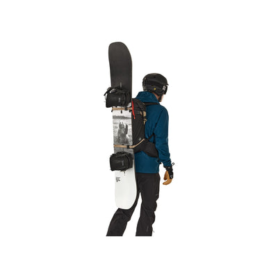 Snowboarder met rugzak draagt snowboard en uitrusting, zijaanzicht op witte achtergrond