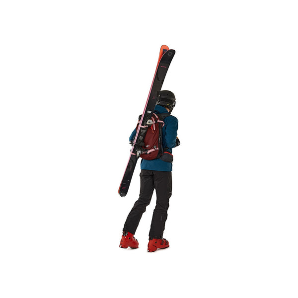 Skiër met ski's op de rug, rugzak en skiuitrusting in blauw jasje en rode schoenen