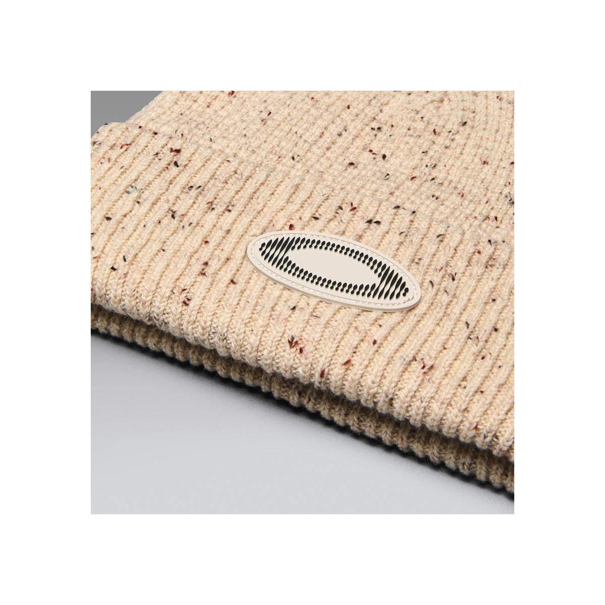 Beige gebreide muts met logo patch, close-up textuurdetail van geribde wollen beanie