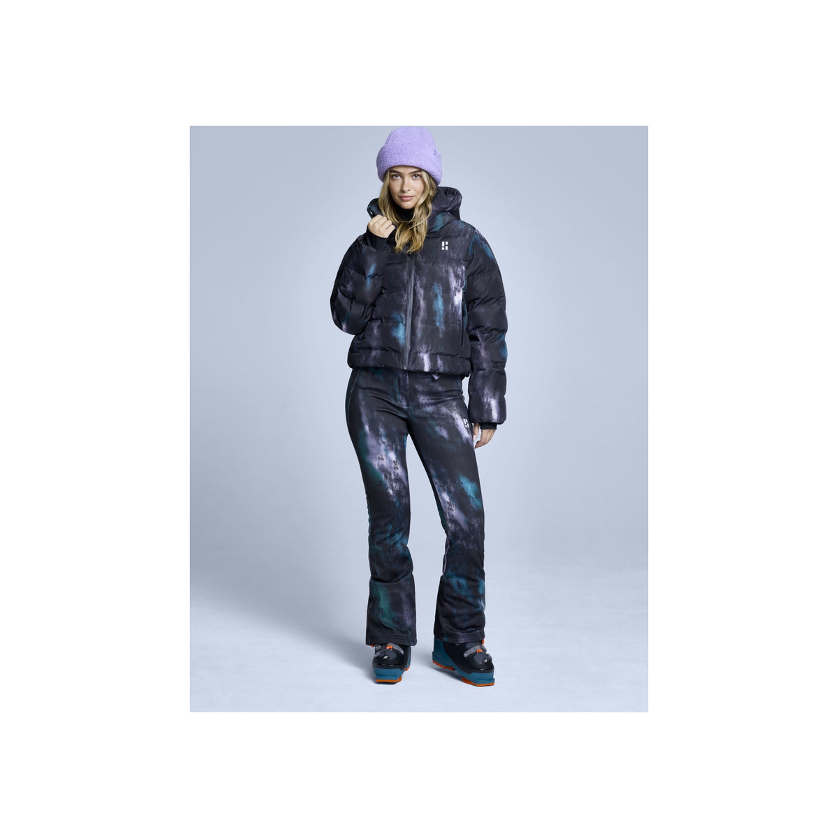 Vrouw in paarse muts met zwart-grijze ski-outfit, winterjas en broek, complete snowboard look