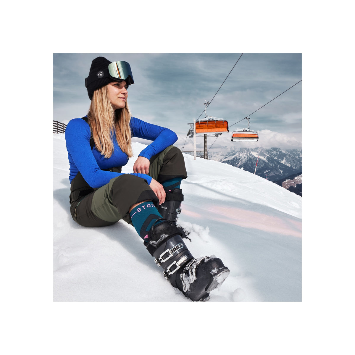 Vrouw zit op de piste met snowboardlaarzen en bindingen, skiliften op de achtergrond in de bergen