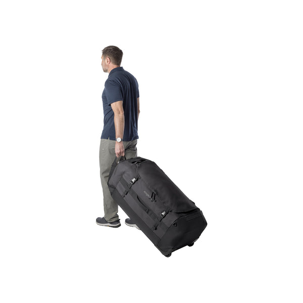 Man trekt grote zwarte roltas met wielen, reisbagage met handgreep voor gemakkelijk vervoer